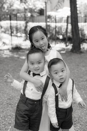Three children in matching formal black and white outfits pose playfully outdoors.