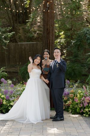 Wedding ceremony in a forest garden setting with flowering purple blooms and string lights among redwood trees.