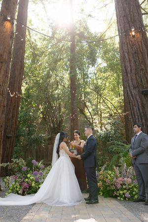 A wedding ceremony taking place in a enchanted forest setting with towering redwood trees and delicate floral arrangements.