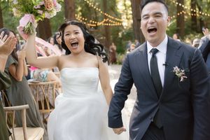 Happy couple walking down the aisle at outdoor garden wedding with fairy lights and pink floral decorations.