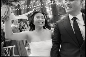 A joyful couple celebrates at their wedding reception under twinkling string lights in black and white.