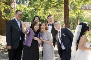 Group of wedding guests and newlyweds sharing a joyful candid moment together at an outdoor garden reception.