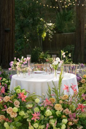 String lights illuminate romantic garden tables decorated with peach roses and pink flowers for an elegant outdoor dinner party.