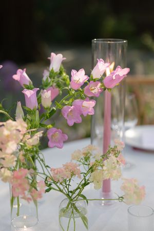 Elegant table settings with pink campanula flowers in glass vases arranged in a row as wedding centerpieces.