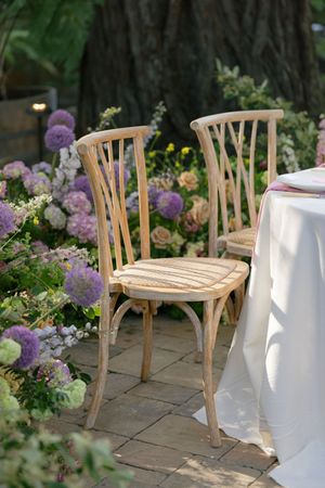 Vintage wooden bistro chairs placed beside purple hydrangeas and garden flowers on a stone patio.
