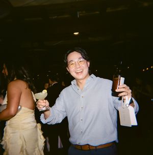 A party guest in a light blue button-up shirt holds drinks and snacks at a festive gathering.