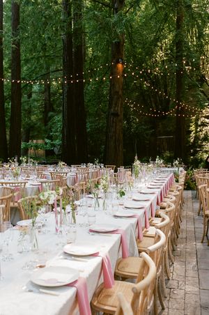 Elegant outdoor wedding reception setup with long tables under string lights in a redwood forest.