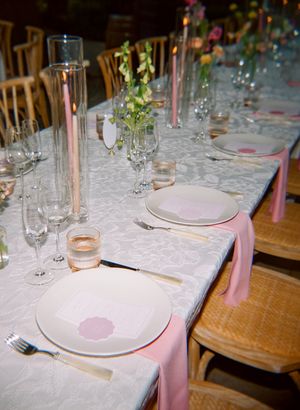 Elegant table setting with white tablecloth, pink napkins, glass candleholders and delicate floral centerpieces.