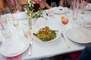A white tablecloth covered dining table set with plates, glasses and colorful dishes of food at a restaurant.