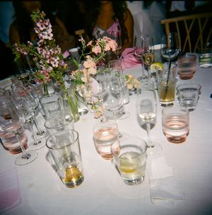 Various drinking glasses with liquid and floral centerpieces decorate an elegant table at a formal event or celebration.