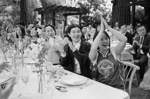 Wedding reception guests celebrate with raised hands and joyful expressions at a table with elegant glassware and place settings.
