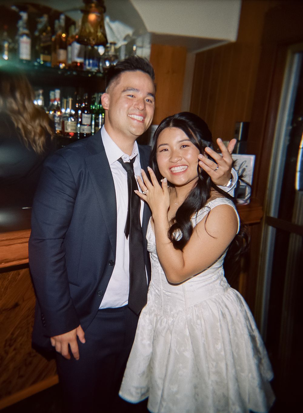 A bride and groom share joyful moments together at their wedding reception, laughing and embracing in formal attire.