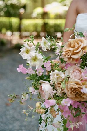 A beautiful floral arrangement featuring peach roses, white lilies and pink delicate flowers against a soft blurred background.