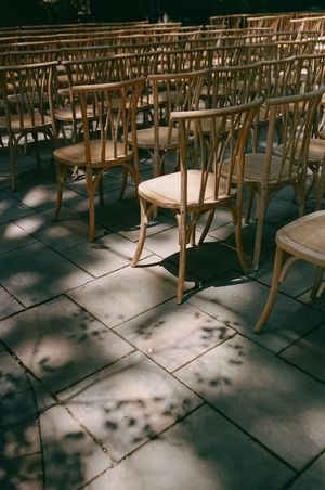 Rows of empty wooden chairs cast dramatic shadows on stone floor in warm vintage lighting.