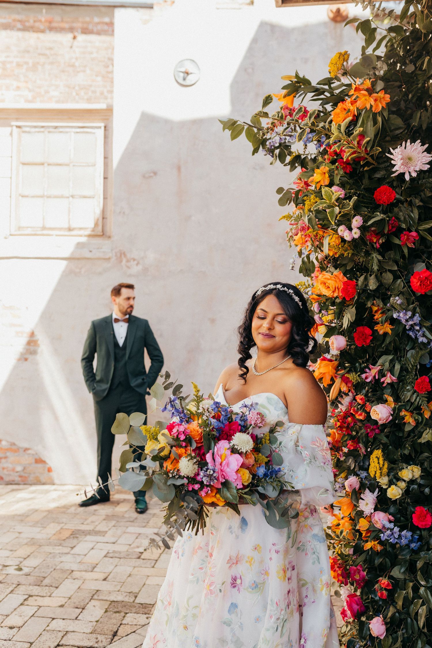 A stunning wedding scene with abundant floral arrangements in orange, red and purple against a white brick wall.