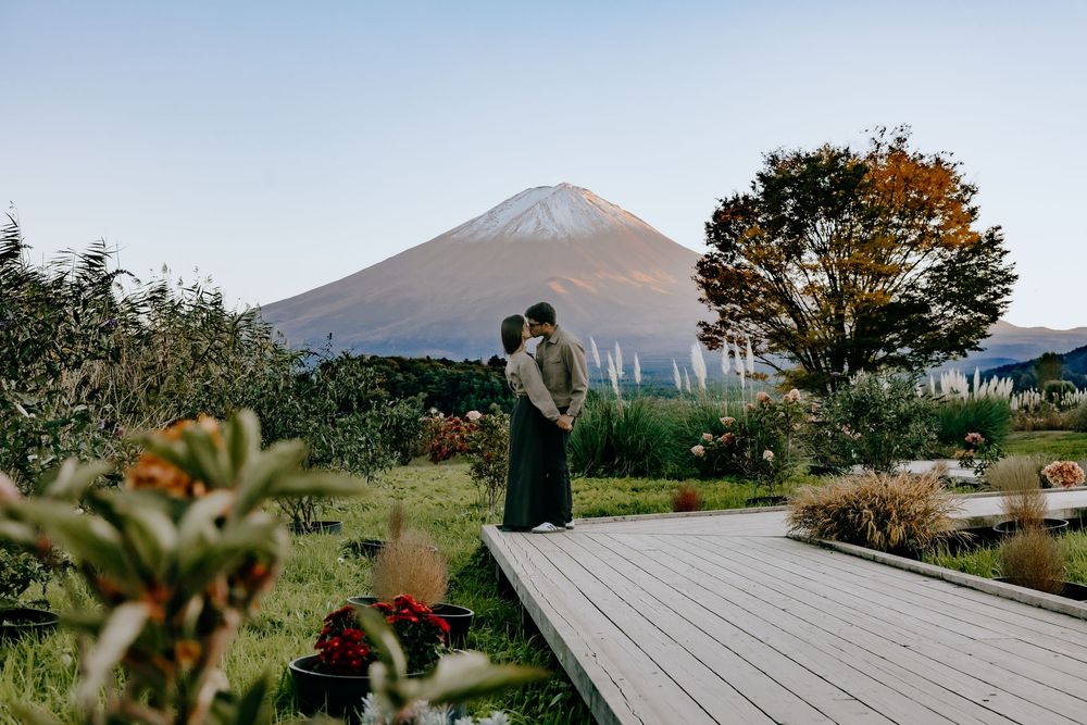 A couple stands on a wooden deck with Mount Fuji rising majestically in the background during golden hour.