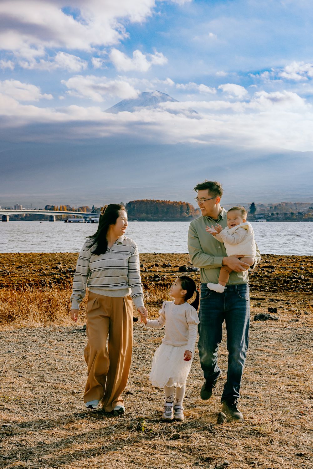 Family enjoying an autumn day together by the waterfront with golden grass and cloudy blue skies in the background.