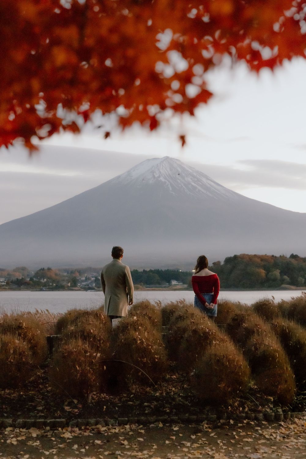 Two people admire the scenic autumn view of Mount Fuji across Lake Kawaguchiko in Japan on a misty day.
