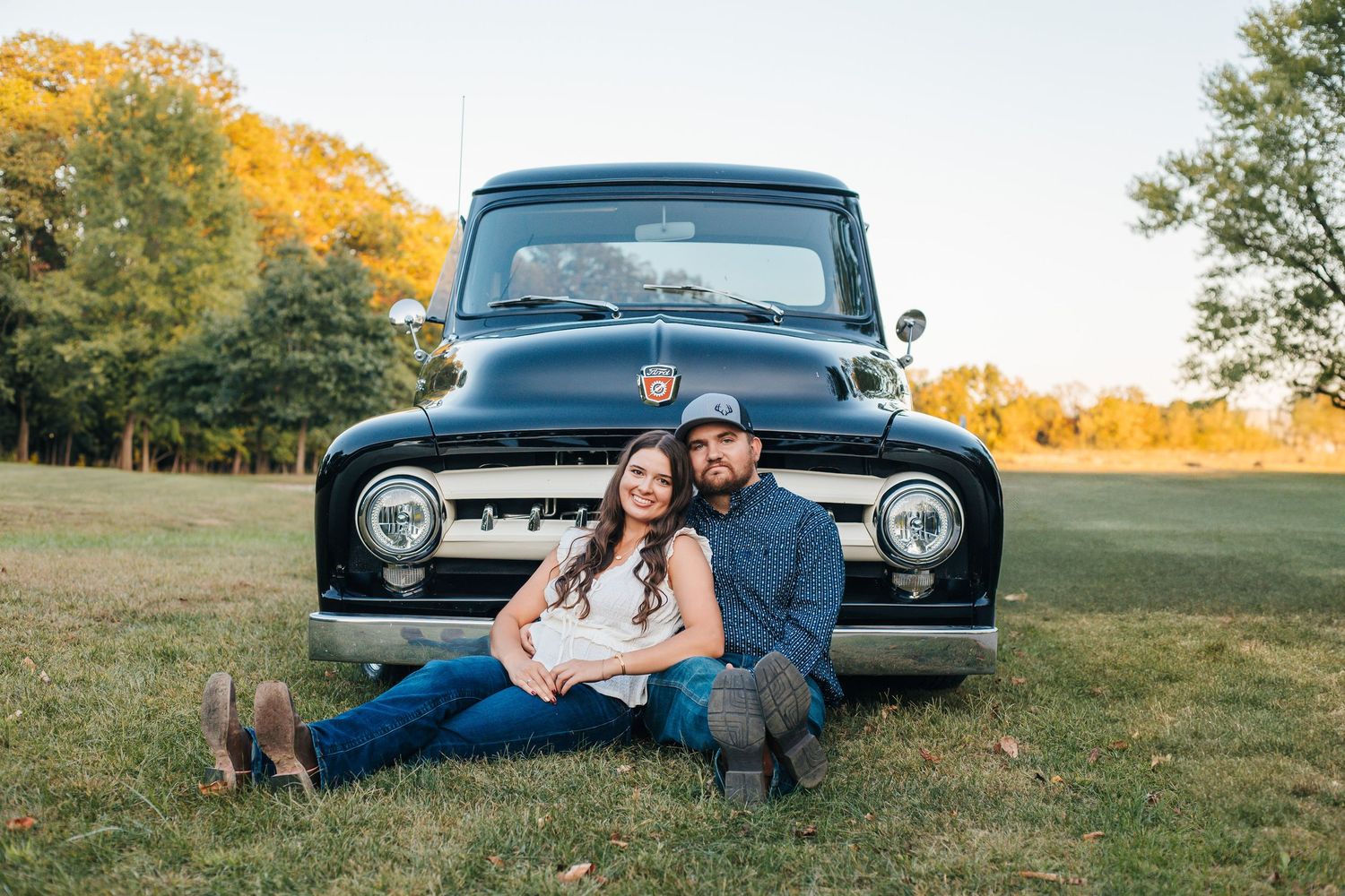 Couple posing together in a romantic fall photoshoot with a vintage blue truck in a grassy field at sunset.