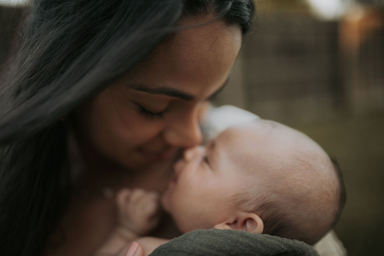 A tender moment captured between two people sharing an intimate kiss outdoors in natural lighting.