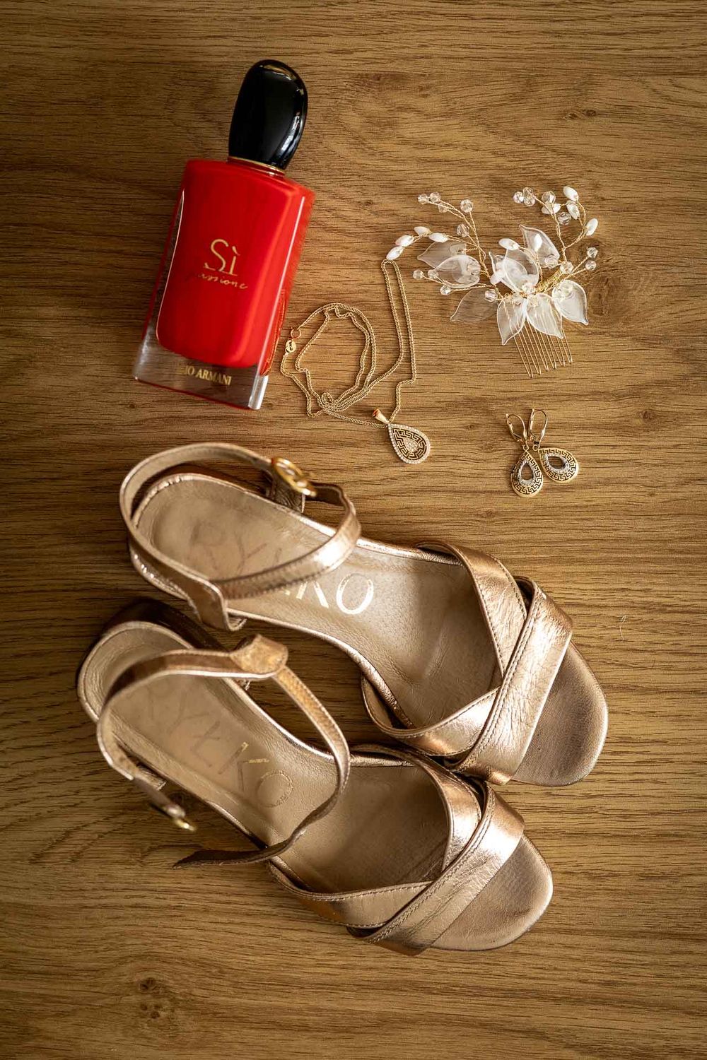 A pair of beige strappy sandals with a red nail polish bottle on a wooden surface with decorative white accents.