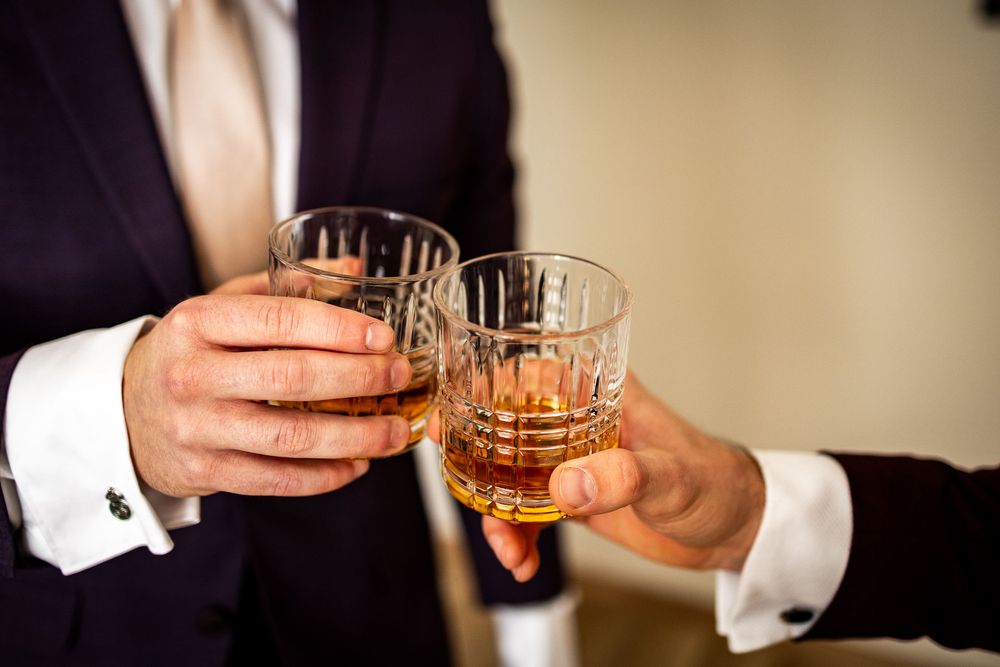 Hands holding crystal glasses filled with amber-colored drinks.