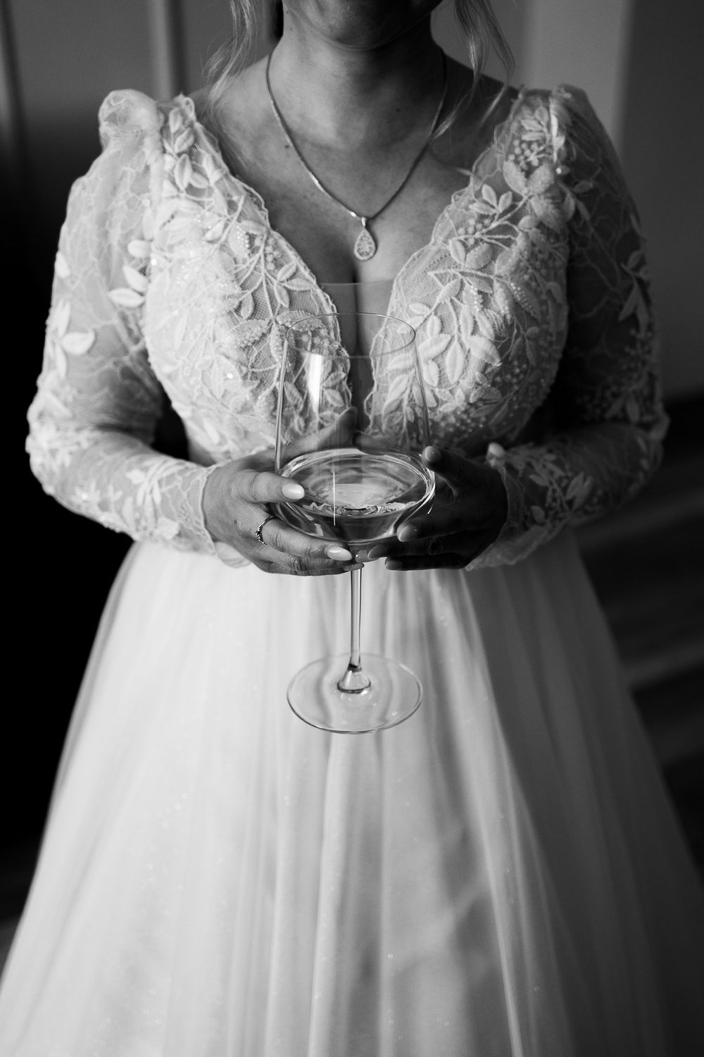 Black and white detail of lace wedding dress with champagne glass.