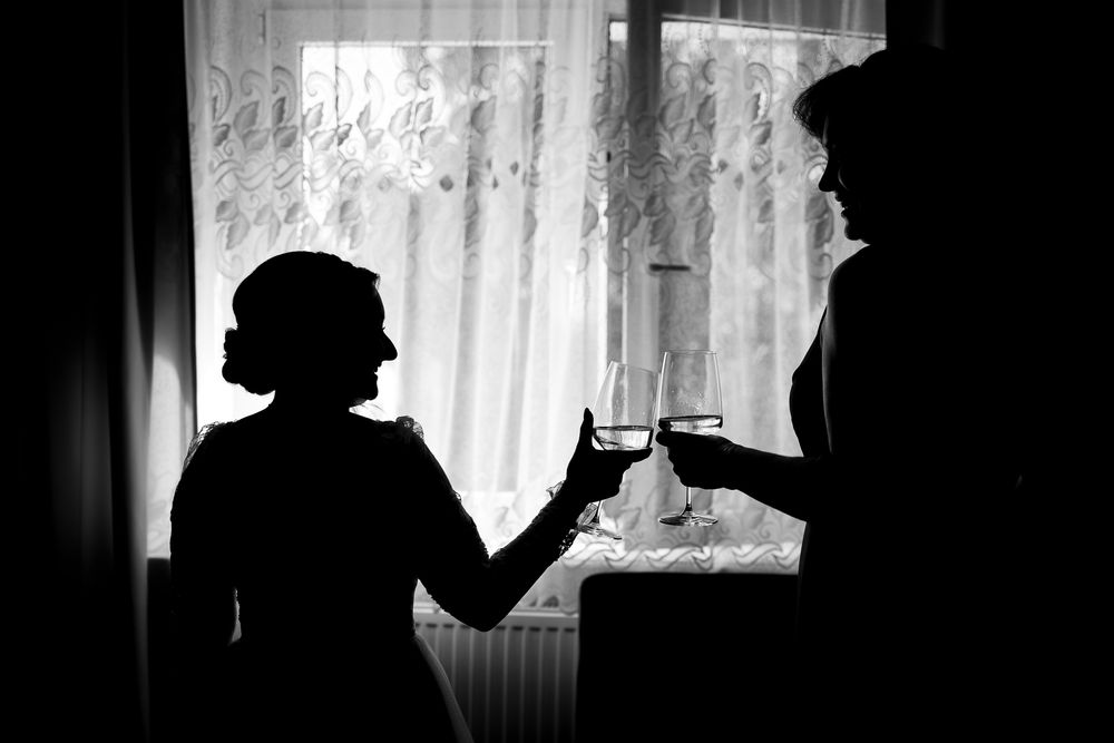 Silhouettes of two people toasting glasses near a window with lace curtains.