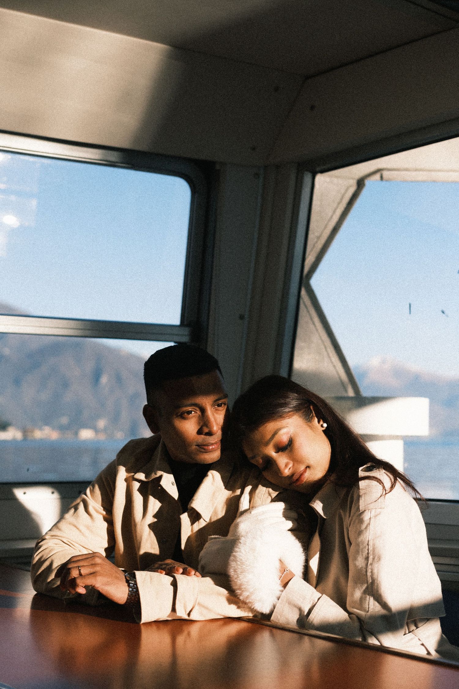 A couple in white outfits rests together on a window ledge with a scenic mountain view in the background.
