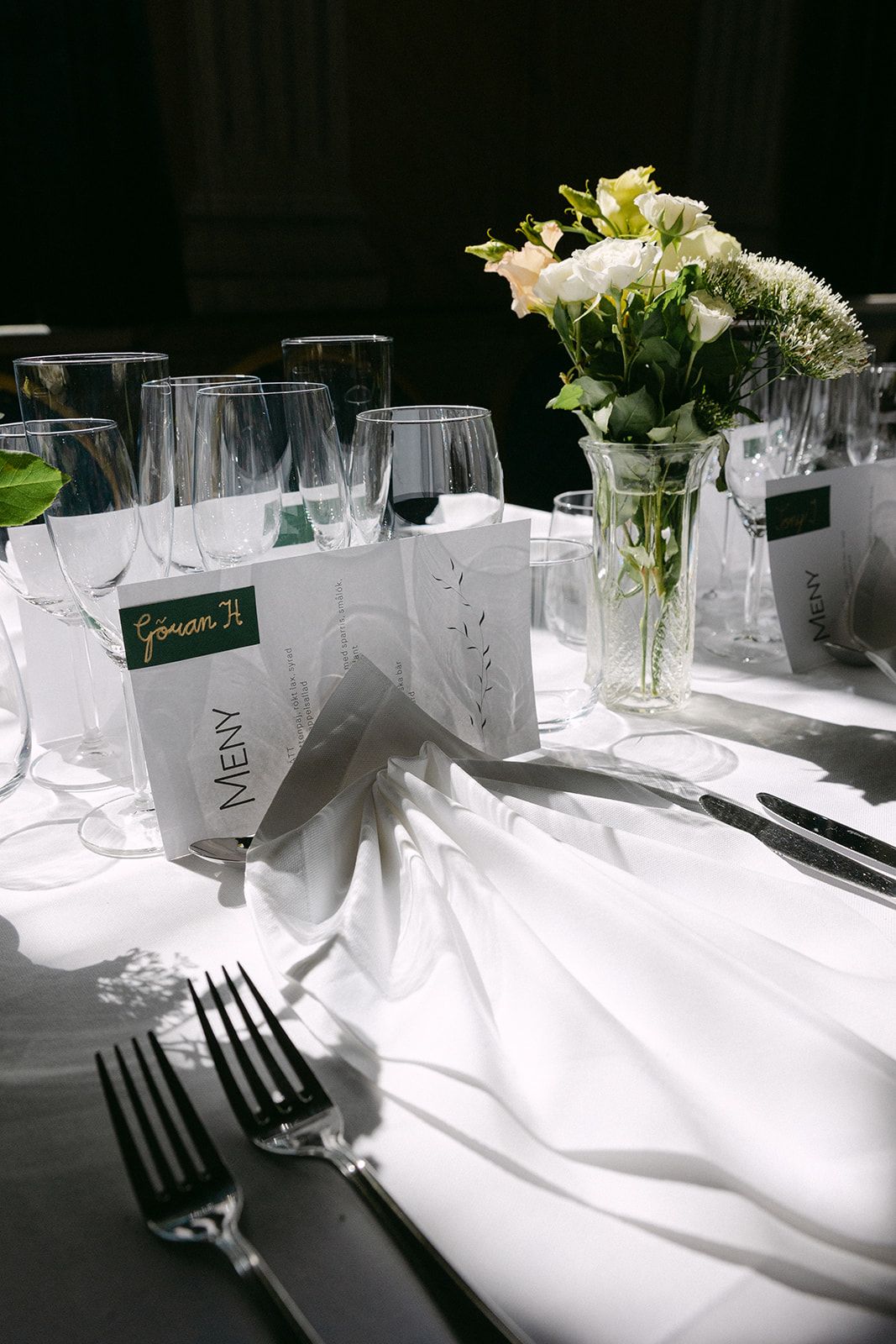Elegant table setting with white linens, wine glasses, menu cards and delicate floral centerpiece in crystal vase.