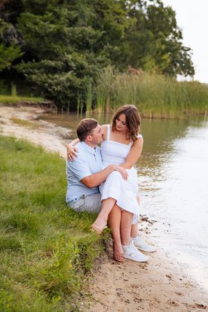 Couple sharing intimate moment on sandy beach shore near calm water.