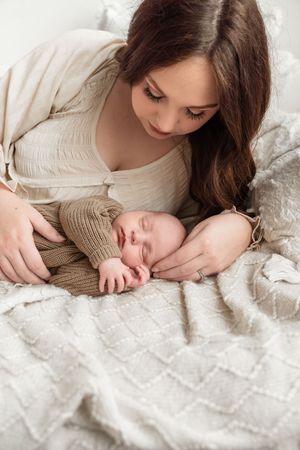 Tender moment between parent and sleeping baby on textured white bedding.