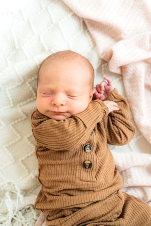 Sleeping newborn baby wrapped in cozy brown knit sweater.