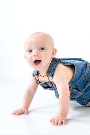 Happy baby in denim overalls crawling on white background.