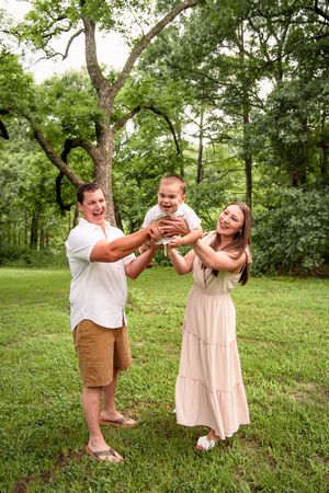 Family playing together on grassy lawn surrounded by lush green trees.