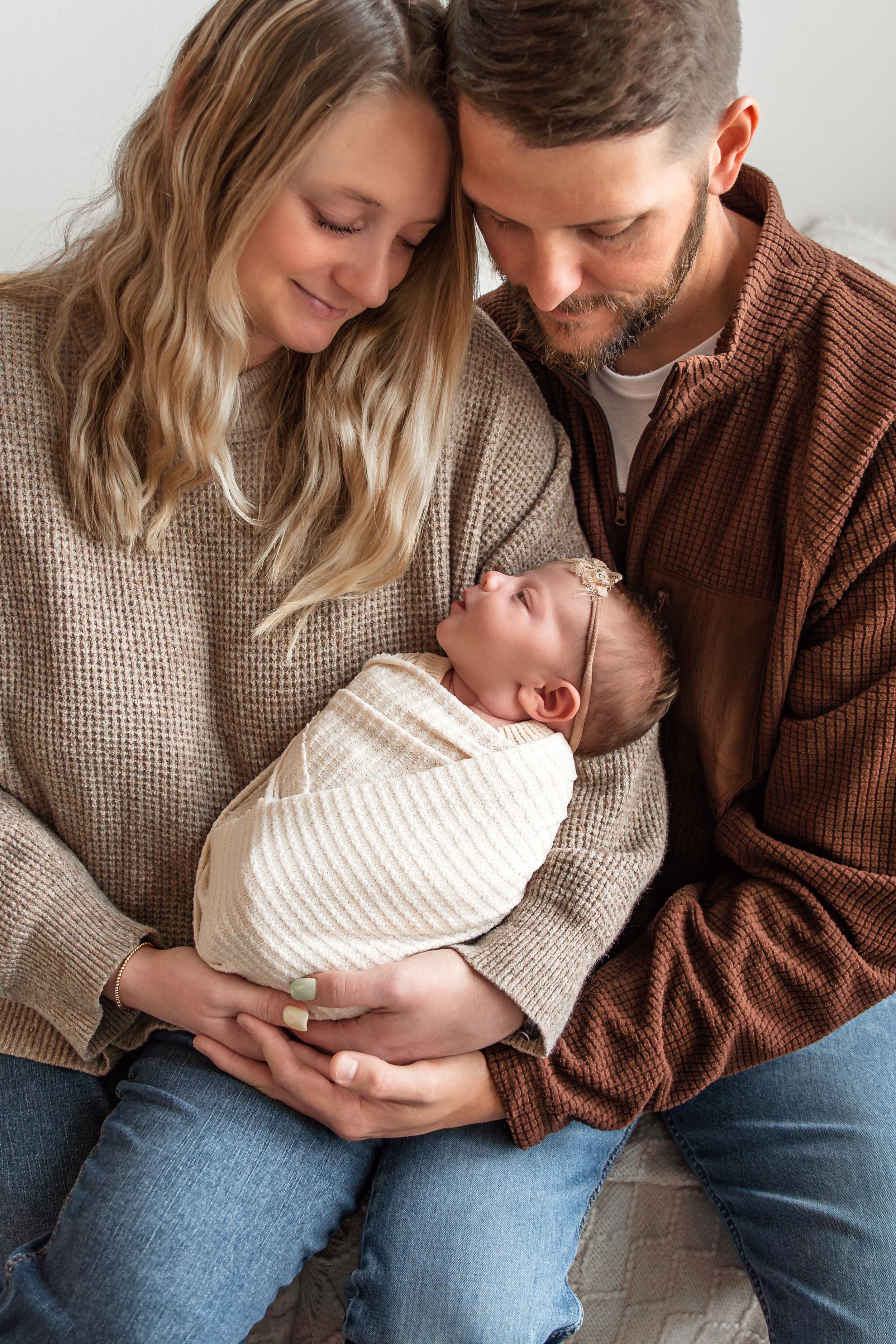 Parents in cozy sweaters sharing tender moments with their newborn in warm lighting.