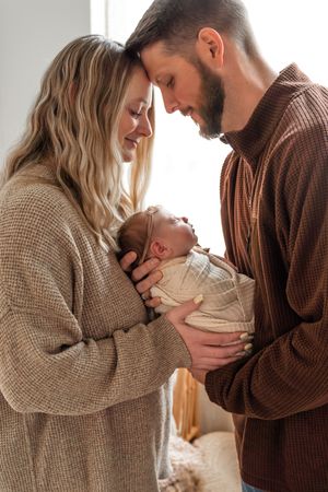 Parents in cozy sweaters sharing tender moments with their newborn in warm lighting.