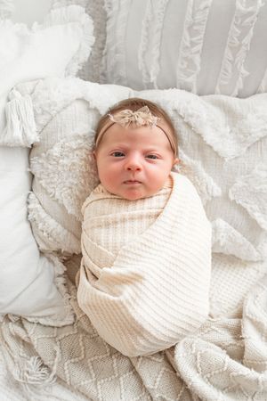 Newborn baby swaddled in soft cream-colored blanket against white lace background.