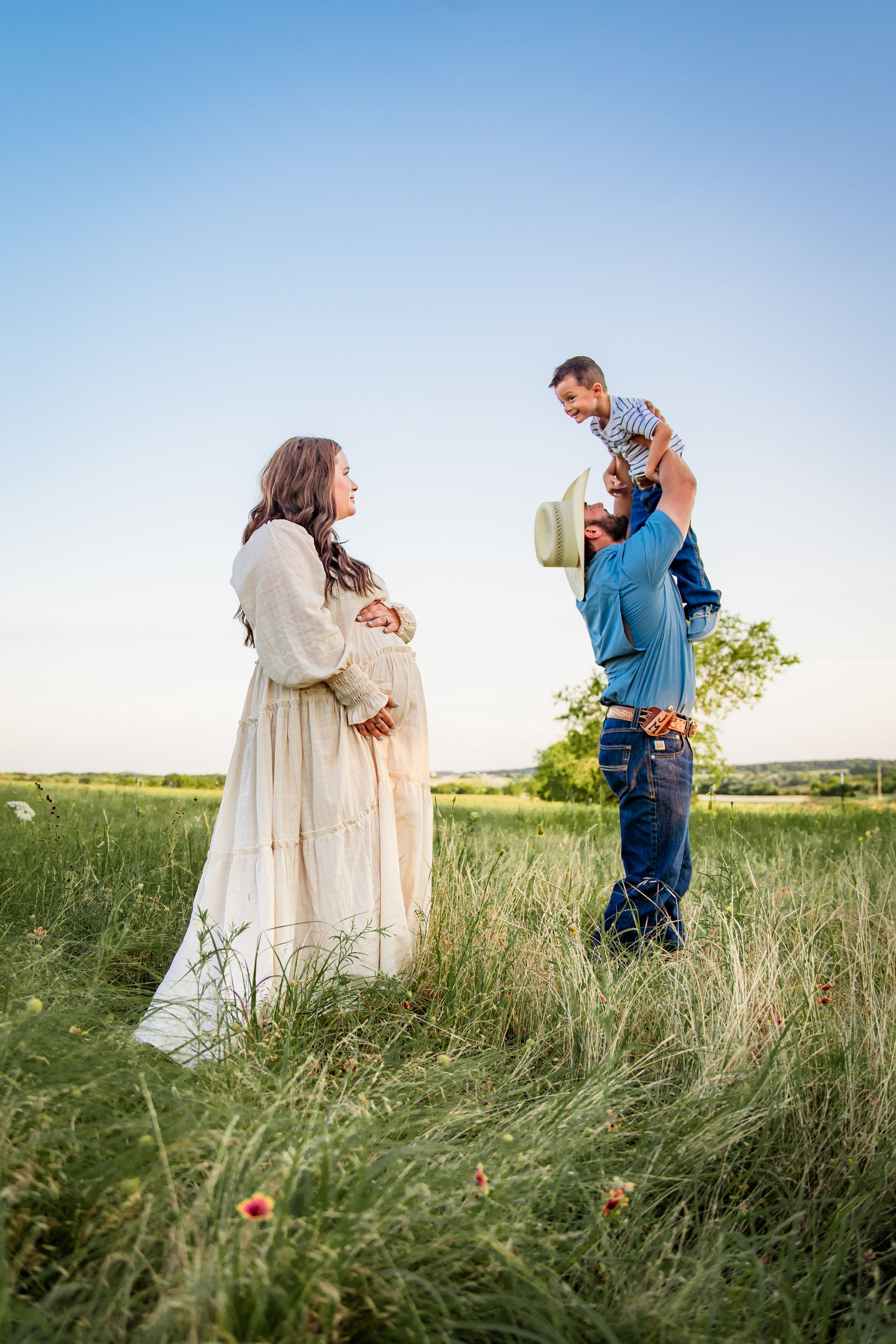 A couple embraces in a serene prairie field during golden hour with tall grass and wildflowers surrounding them.