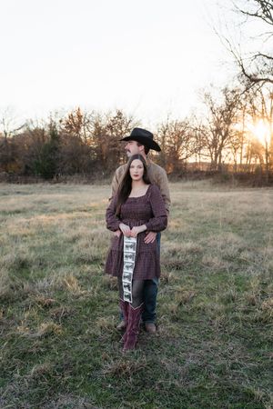 Woman in plaid dress poses in field during golden hour sunset.