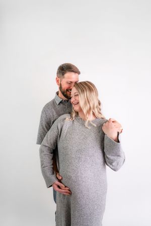 Intimate portrait of couple in matching grey outfits against white background.