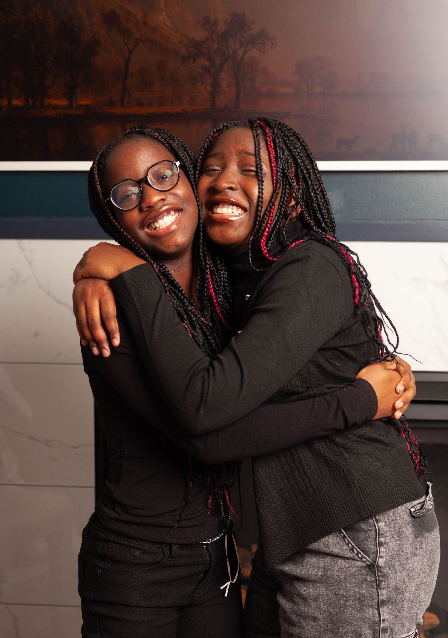 Two people in black sweaters share a warm embrace and joyful smiles against a dark background.