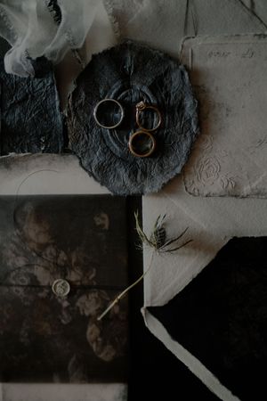 Wedding rings rest on dark textured surfaces in a series of moody, artistic detail shots with dramatic lighting.