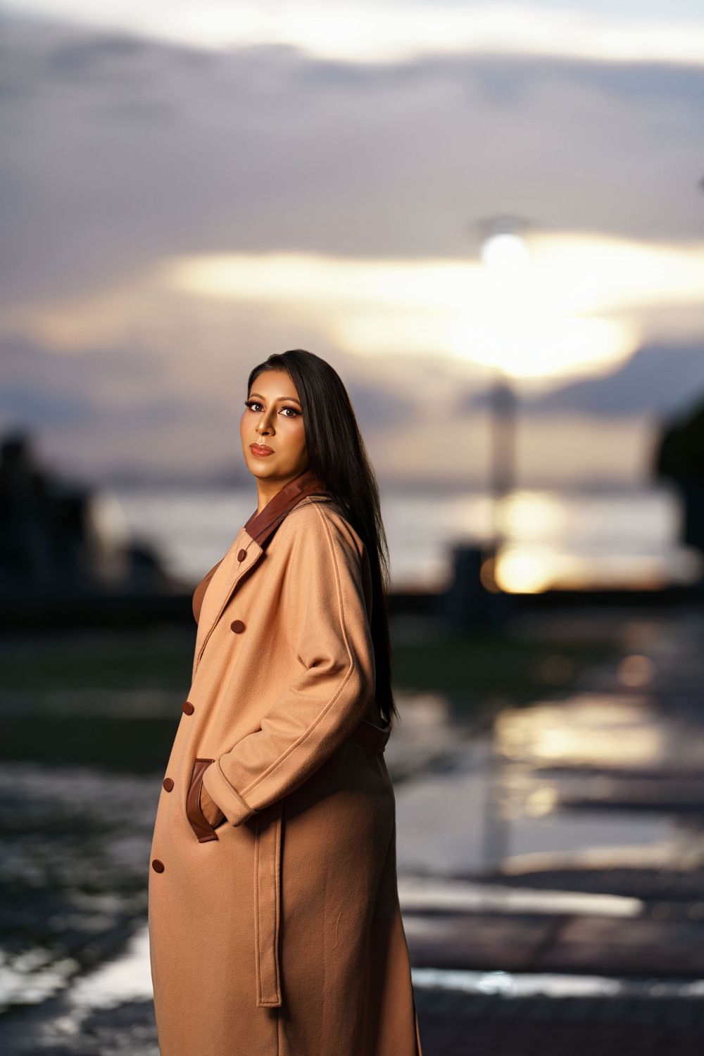 A series of artistic sunset portraits showing a figure in a beige coat against dramatic evening skies and water reflections.