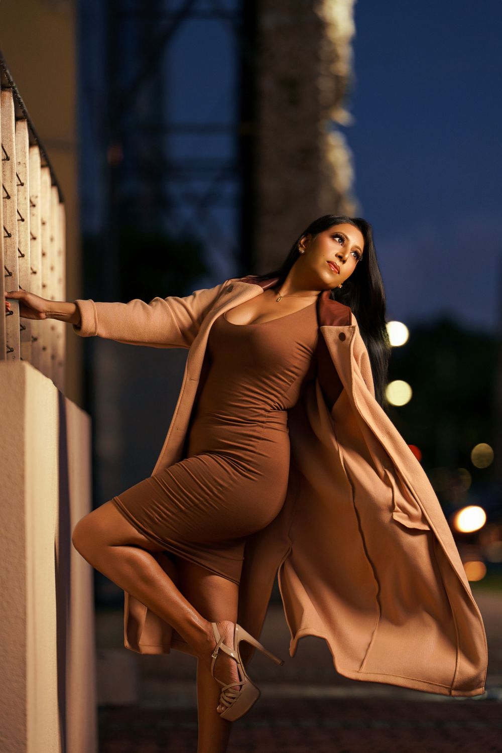Maternity photo shoot at dusk with woman in brown bodysuit and flowing fabric against architectural columns.
