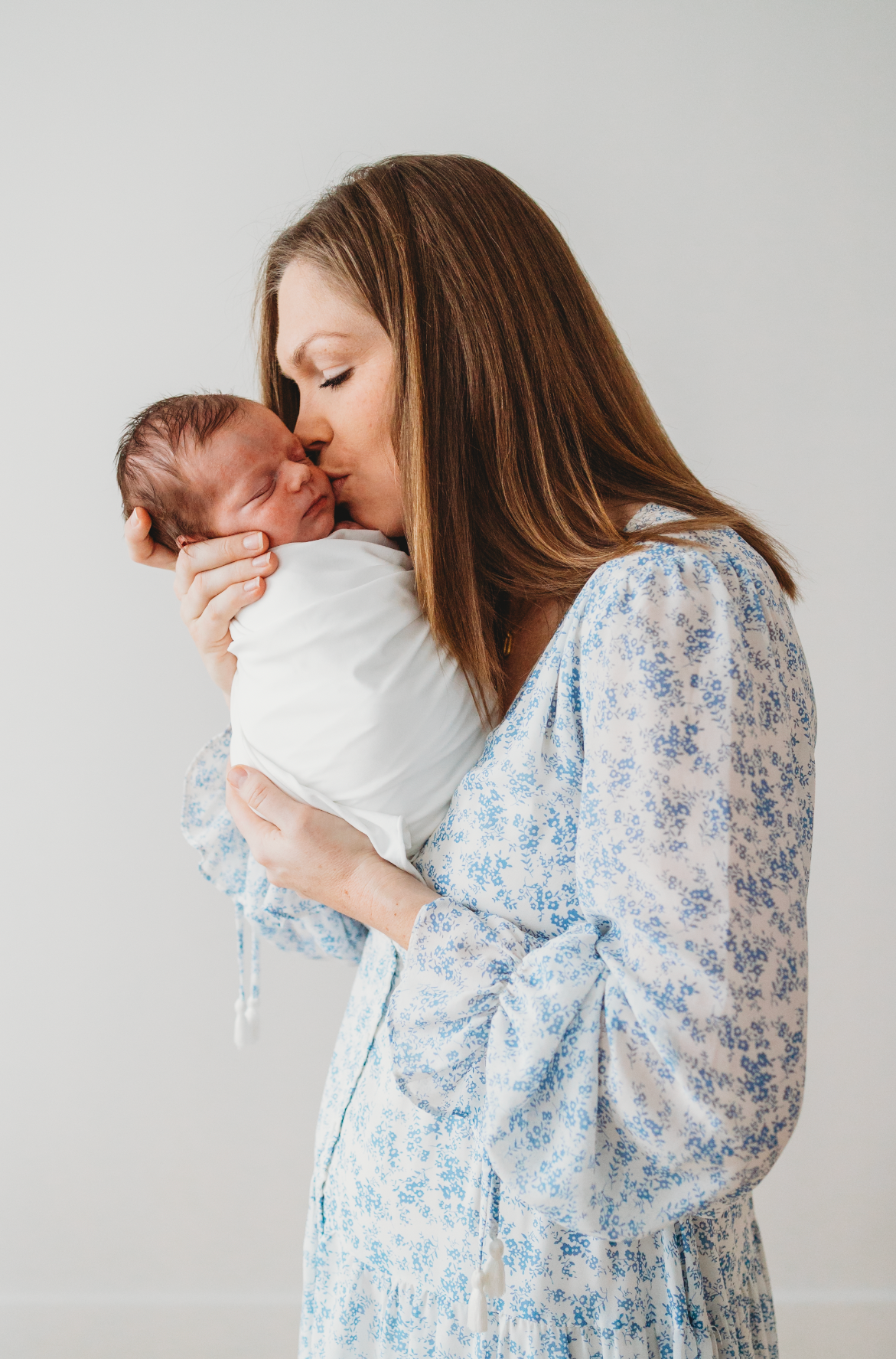 A tender moment captured in a series showing someone in a blue floral dress holding and snuggling a small baby.