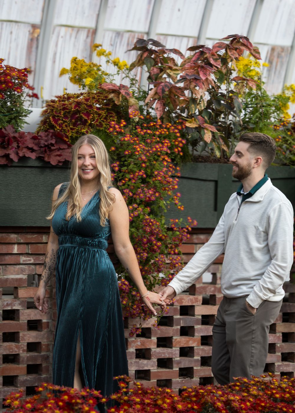 A couple poses playfully against a backdrop of colorful autumn flowers and wooden lattice.
