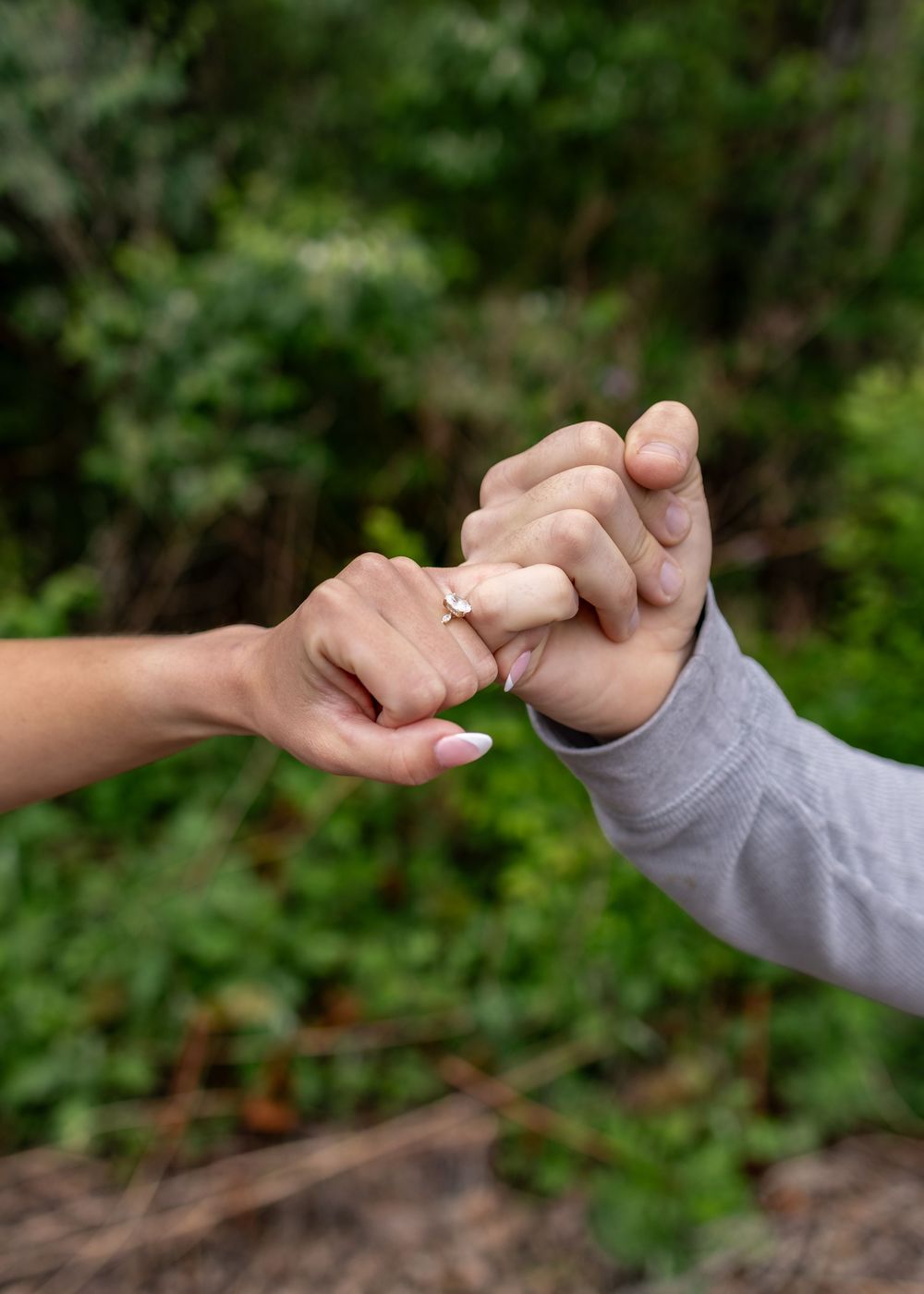 Close-up of a couple holding pinkies outdoors, woman wearing a delicate engagement ring on her finger.