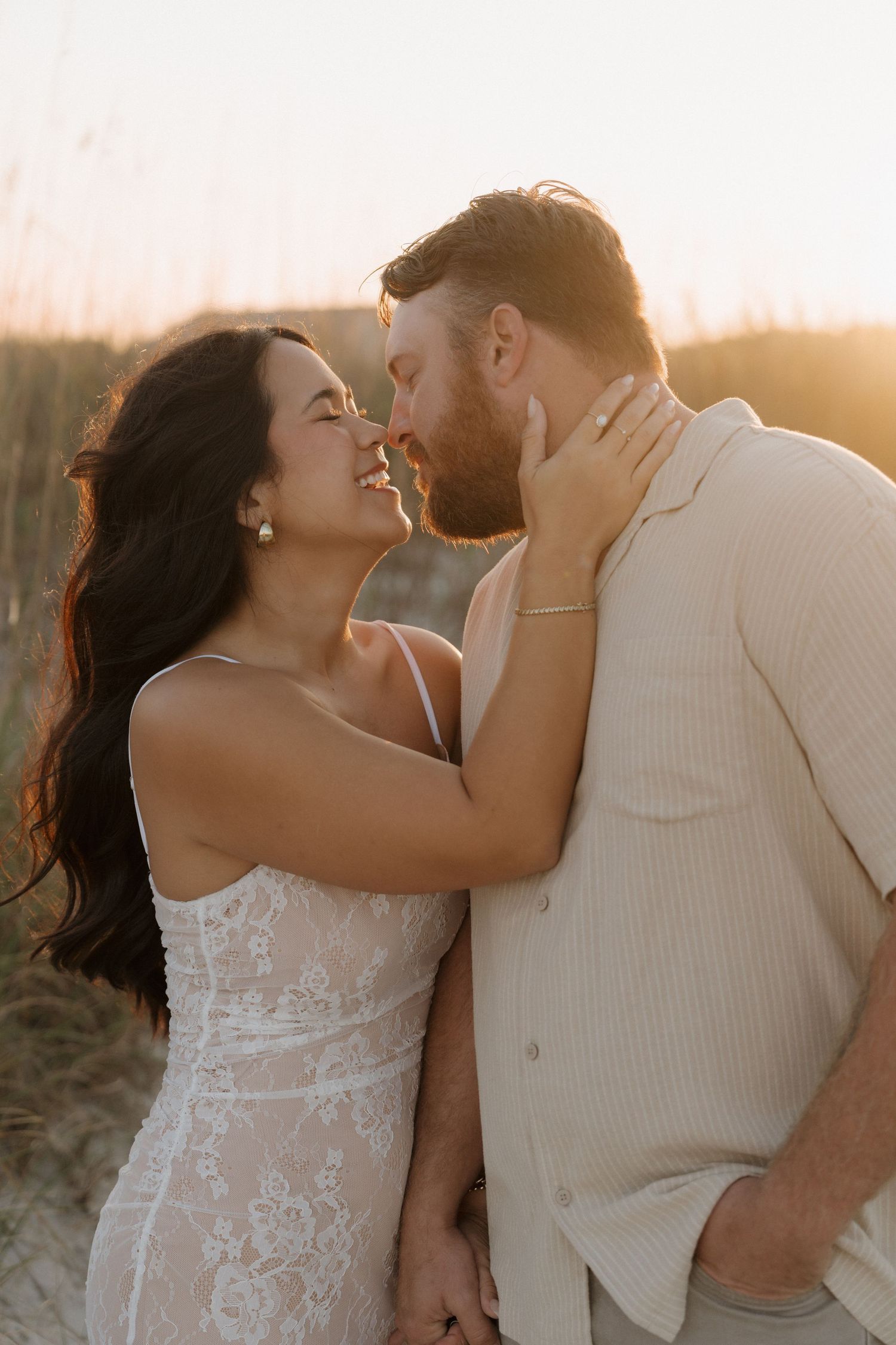A romantic couple embraces and kisses during golden hour sunset in an outdoor setting.