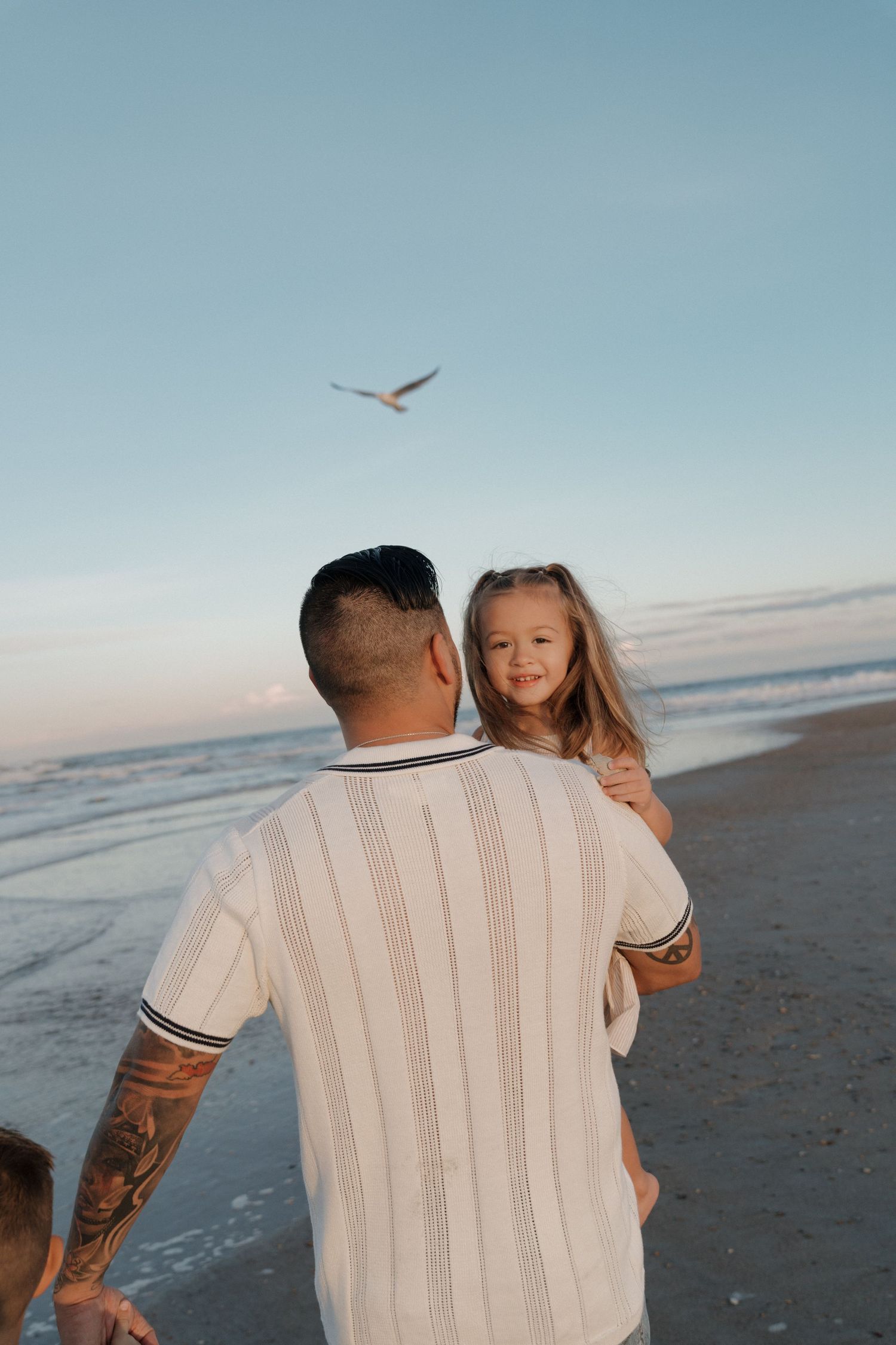 A heartwarming beach scene at sunset with people enjoying the ocean waves and seabirds flying overhead.